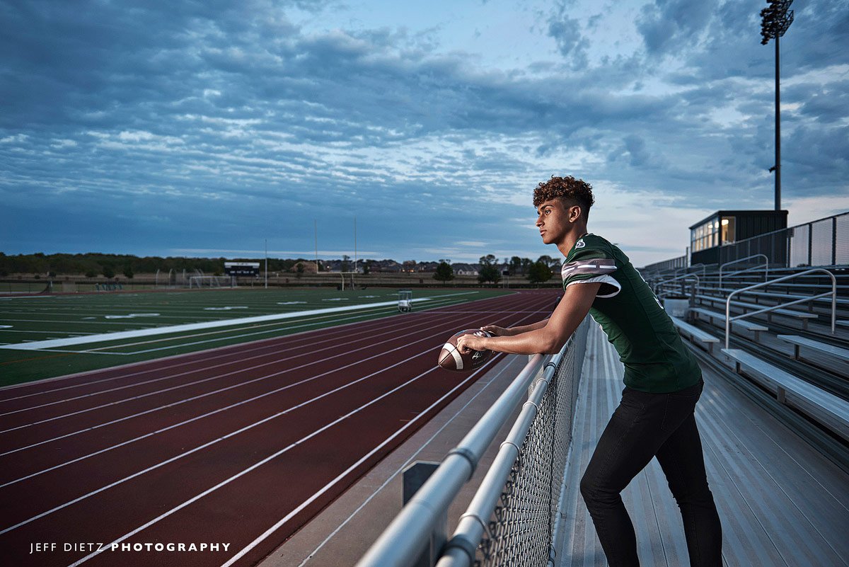 prosper football player stands in the bleachers overlooking the field for senior portraits