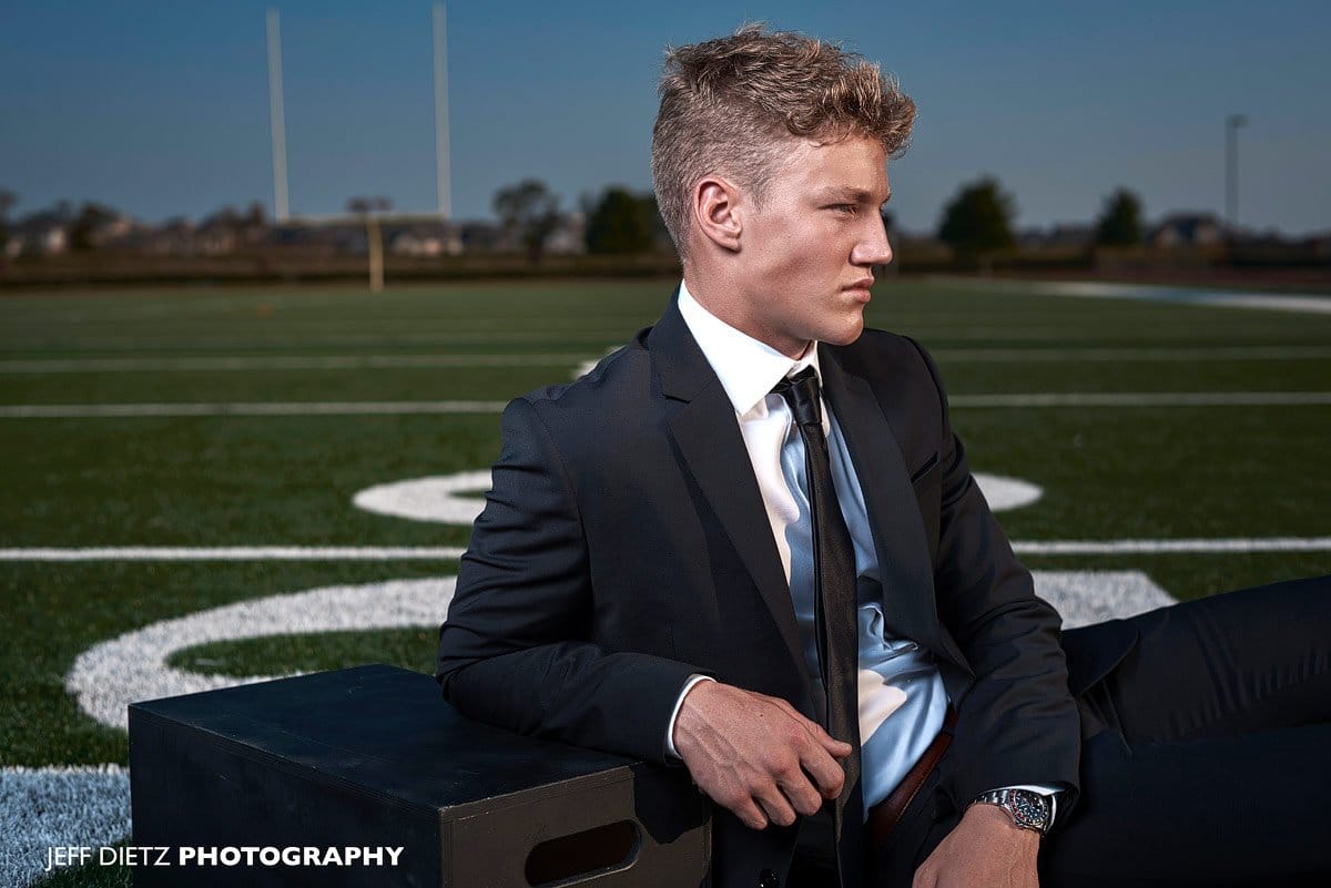 Prosper football player poses for senior portraits on prosper high practice field in suit
