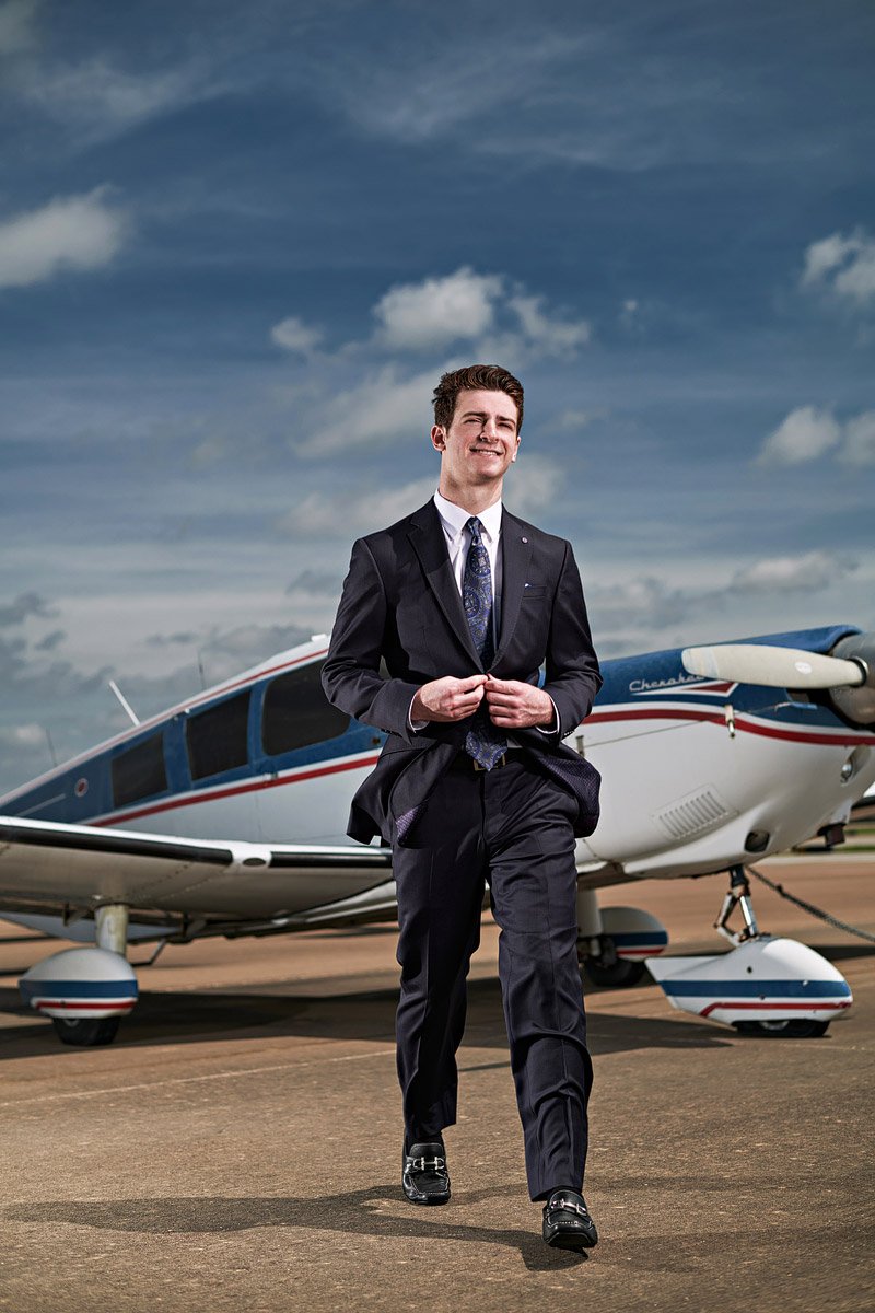 prosper senior photographer student walking away from airplane in suit